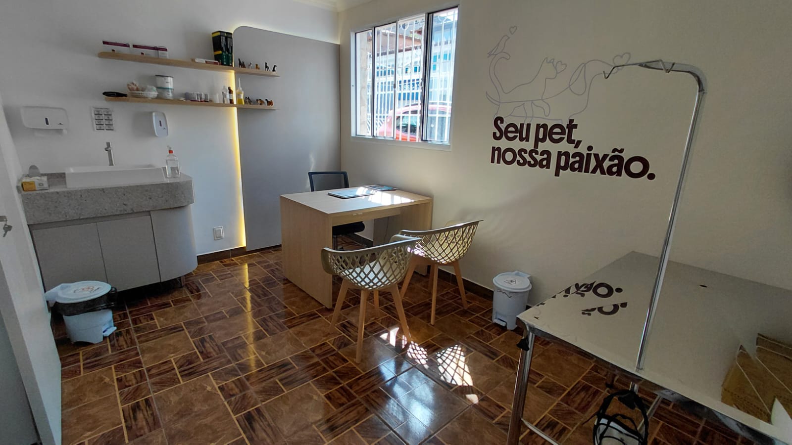 Consultório Cães, possui um painel de madeira com led, mesa de atendimento e avaliação, uma balança para pesagem.