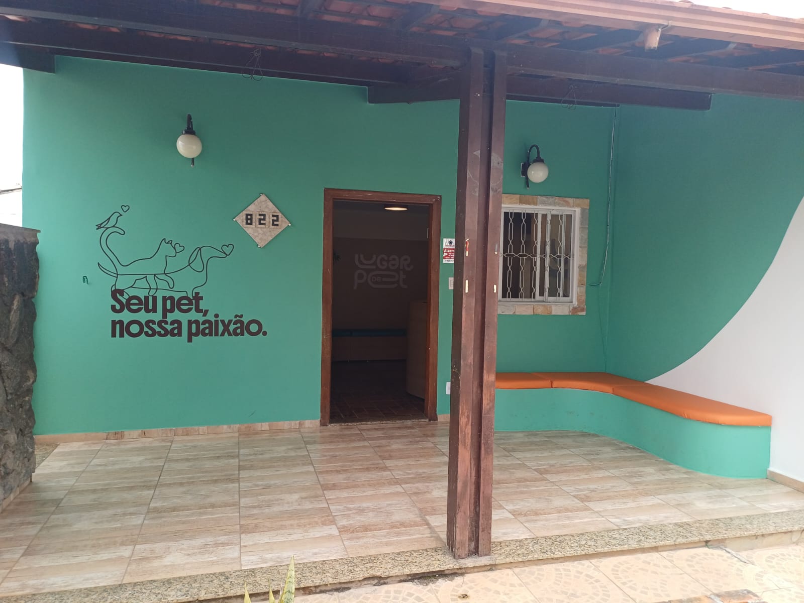 Fachada interna, com banco de espera considerado como sala de espera externa. Aparece um banco, puffs e o destaque na pintura da fachada que é no tom verde turqueza